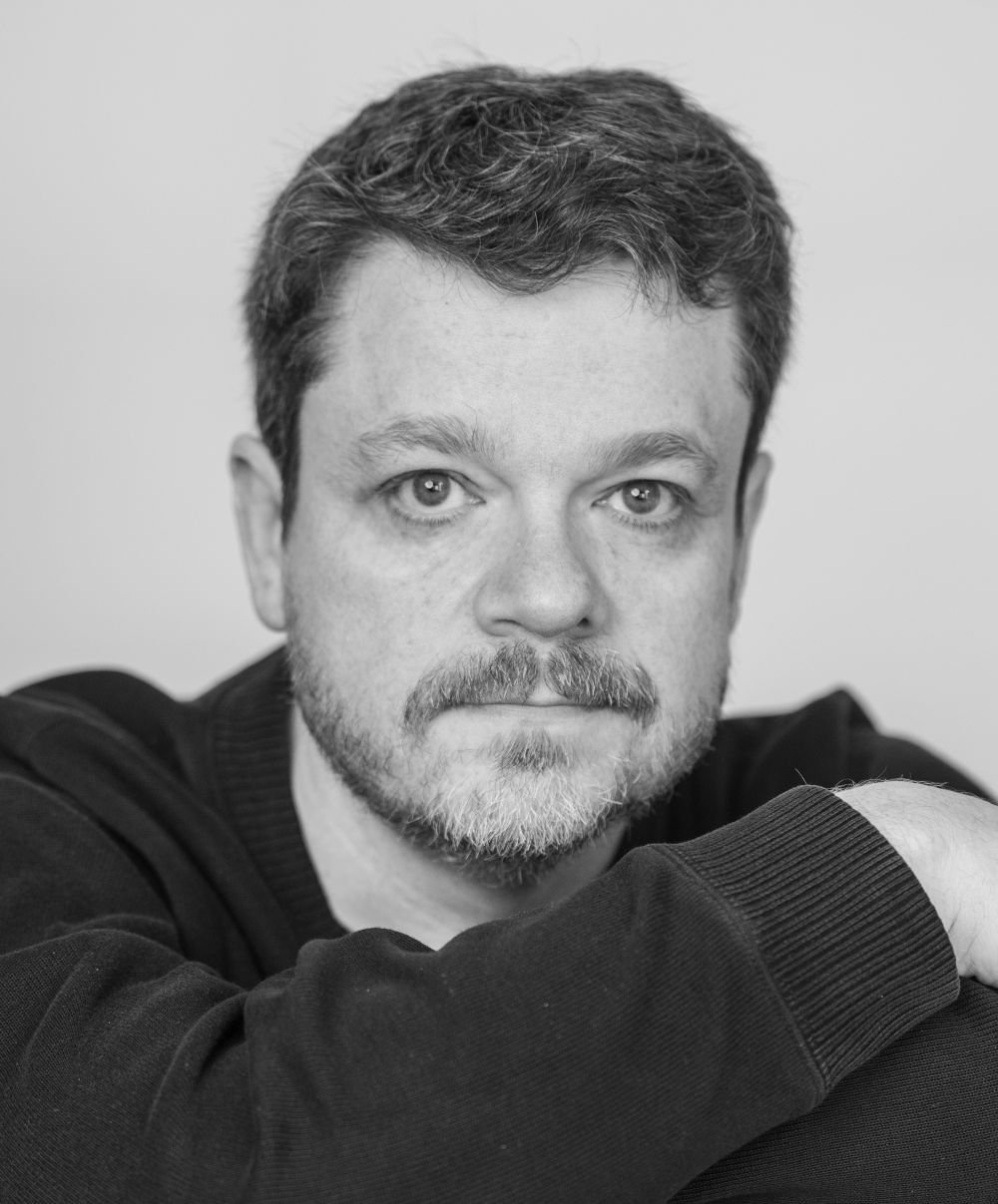 A black and white photo of a white man looking directly at the camera.