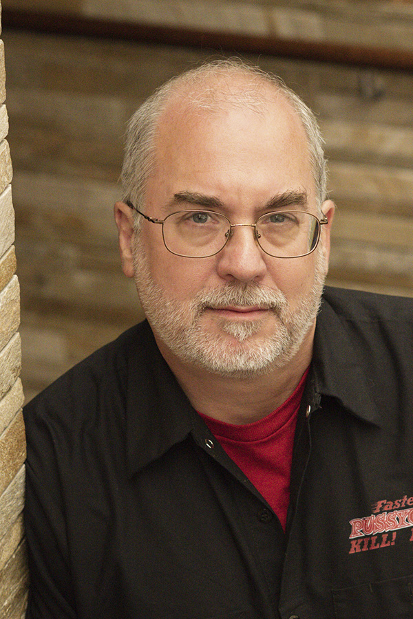 A balding white man with glasses looks directly at the camera.