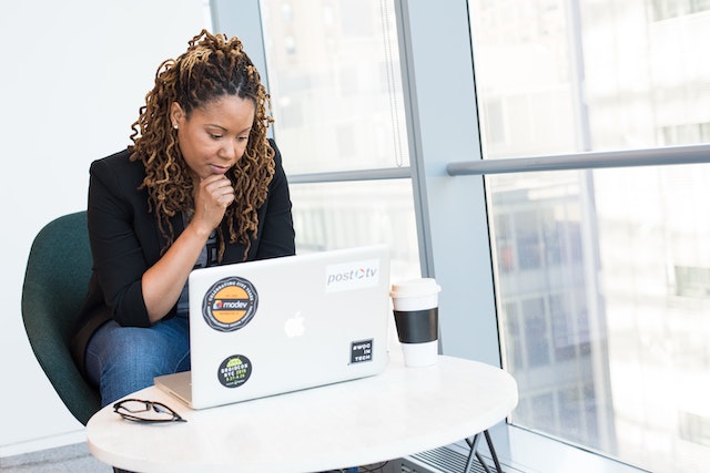 A black woman with locs sits in front of a laptop looking pensive.
