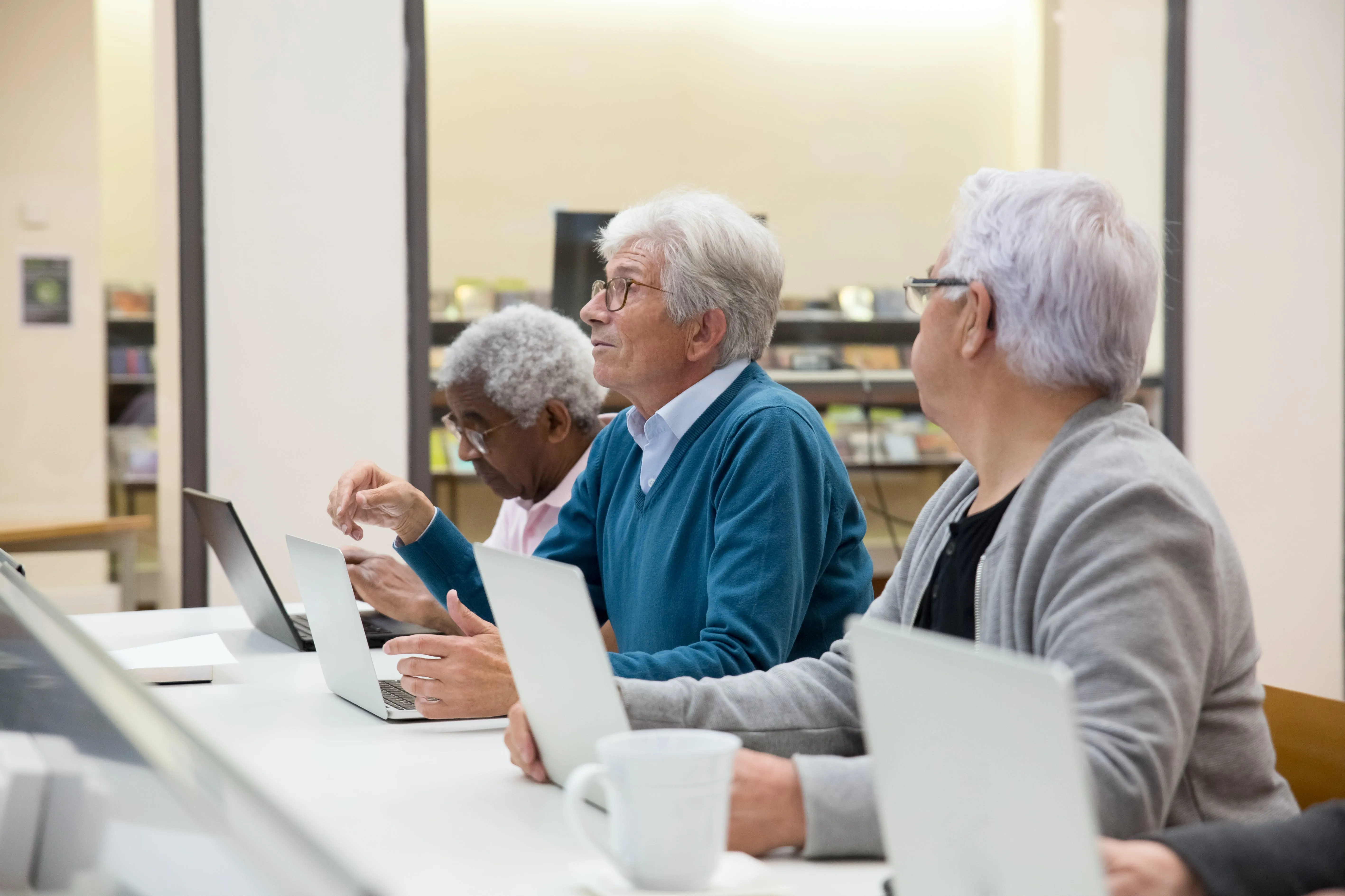 A group of three seniors sit at computers learning about them.